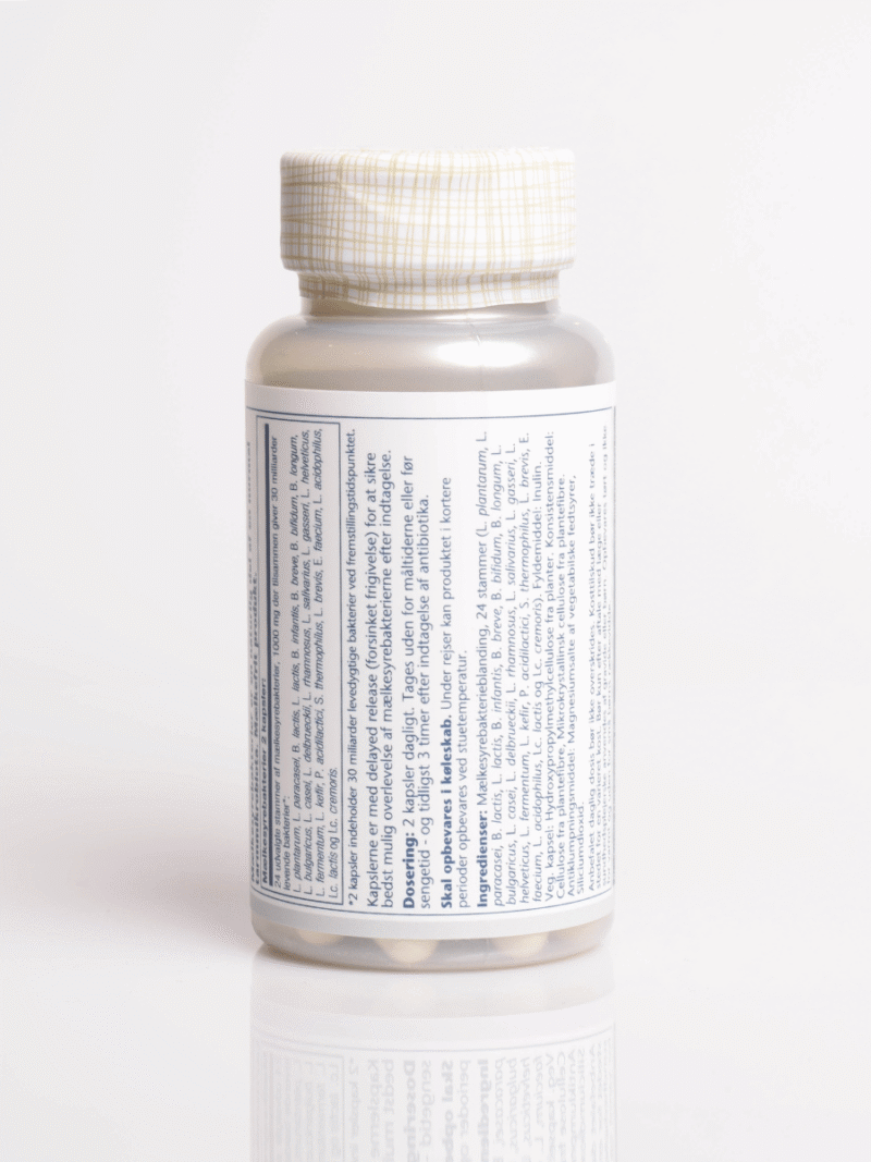 Hvid kosttilskudsflaske med gittermønstret låg, detaljeret dansk label og synlige tabletter i bunden, på hvid baggrund