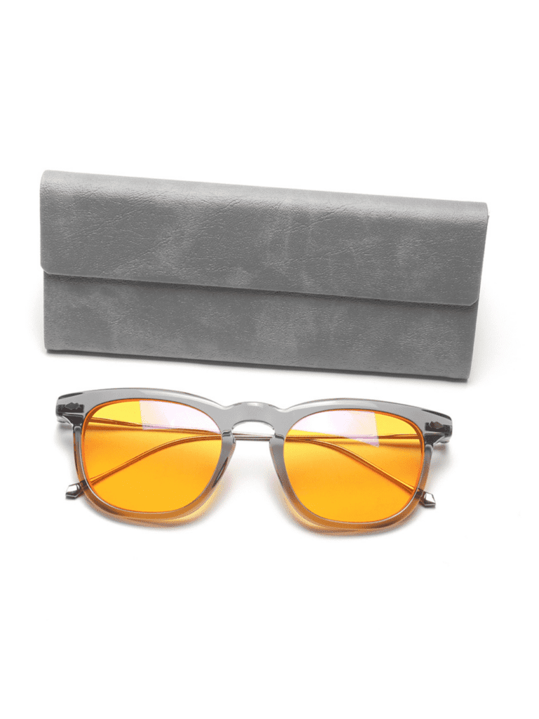 Retro-Sonnenbrille mit orangefarbenen Gläsern und transparent grauem Gestell vor einem weichen grauen Etui