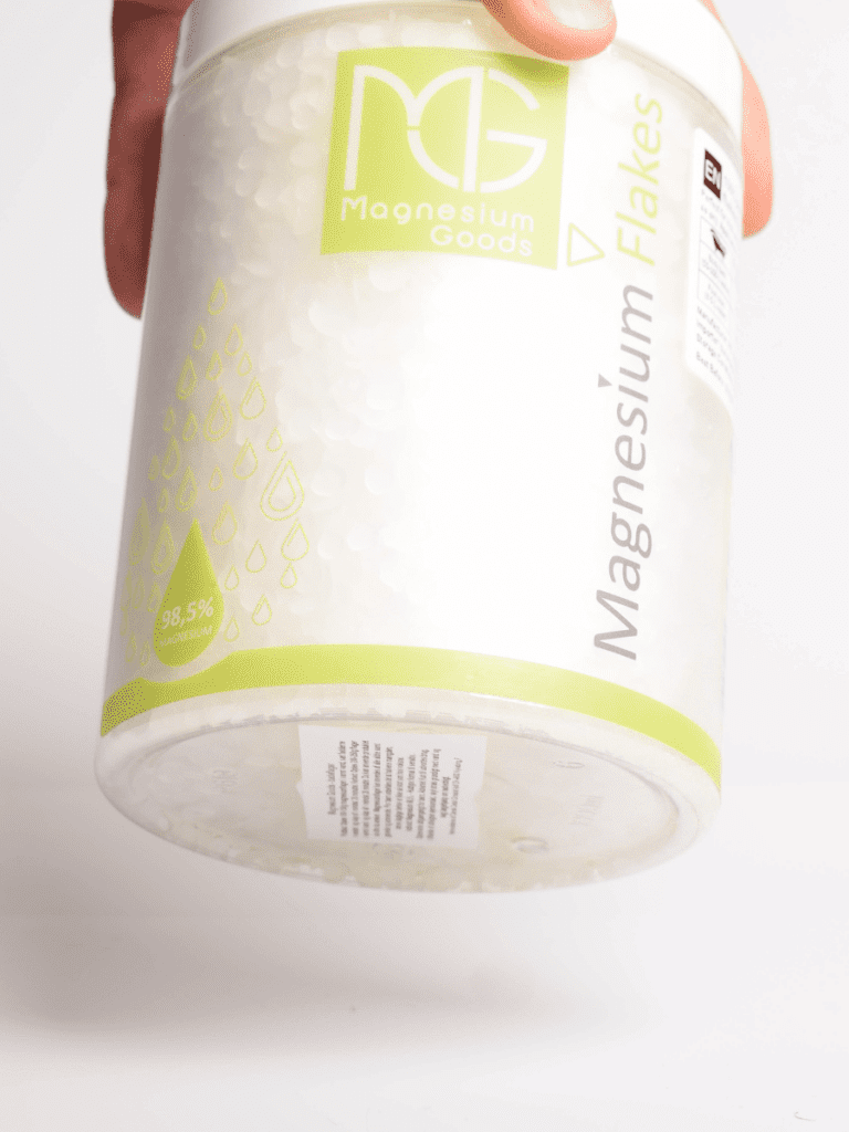 Hånd holder beholder med Magnesium Goods Magnesium Flakes, hvide flager og grøn etiket