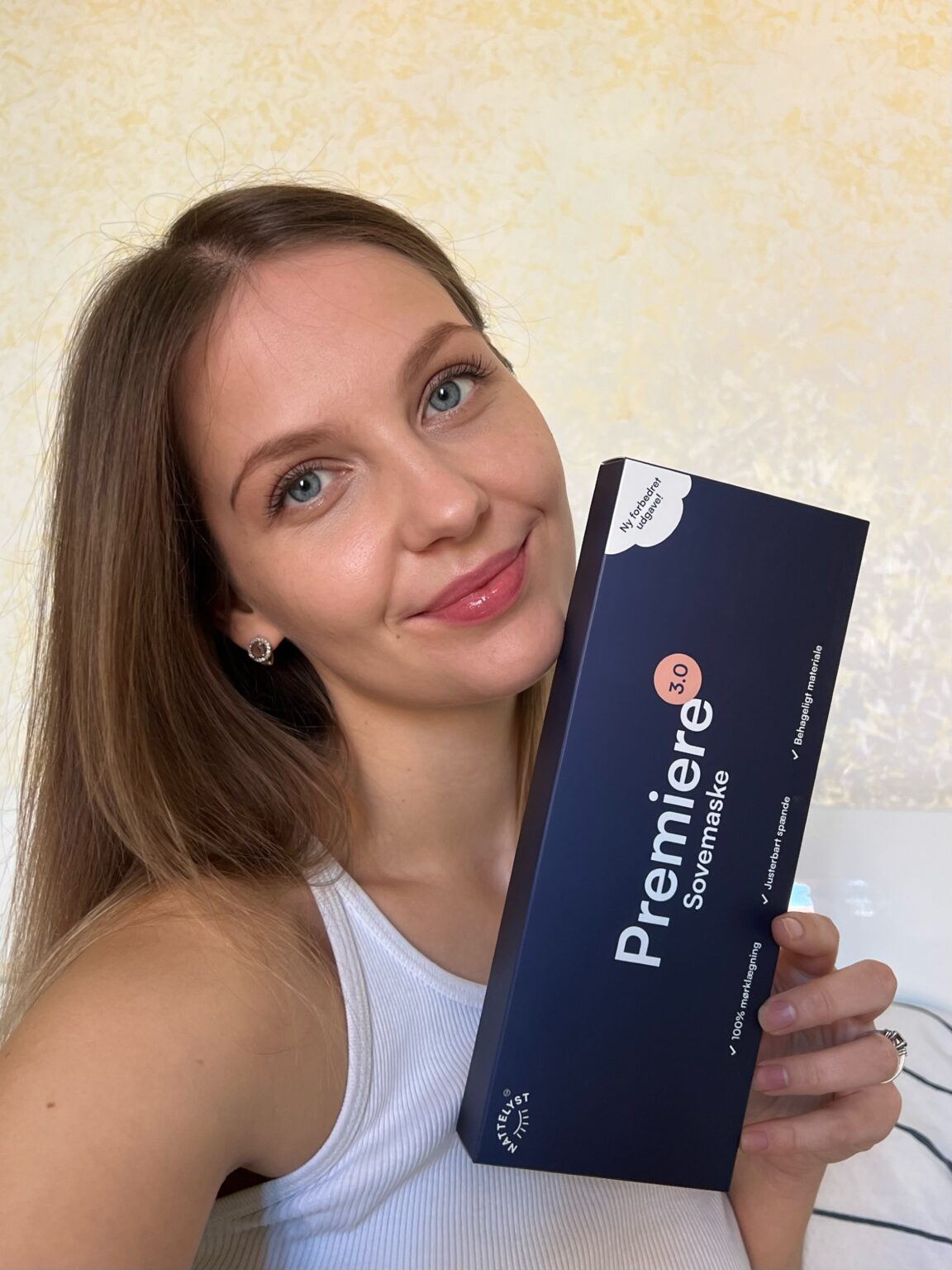 Lächelnde Frau hält die blaue Verpackung der Premiere 3.0 Schlafmaske nah ans Gesicht