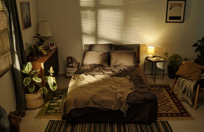 Sonnendurchflutetes Schlafzimmer mit Doppelbett, Plaid, Jalousien, Pflanzen und warmer Nachttischlampe