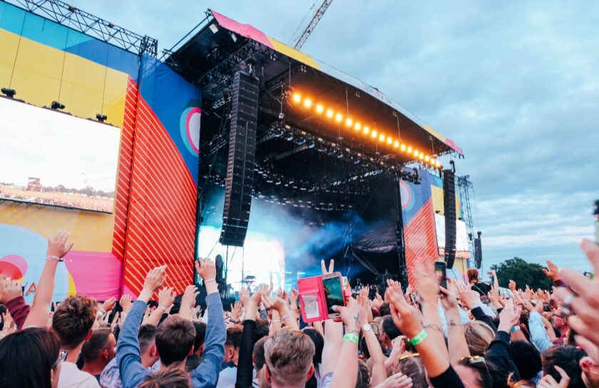 Große Open-Air-Festivalbühne unter Abendhimmel, Publikum mit erhobenen Händen