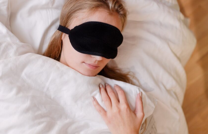 Schlafende Frau mit schwarzer Schlafmaske unter einer weißen Bettdecke