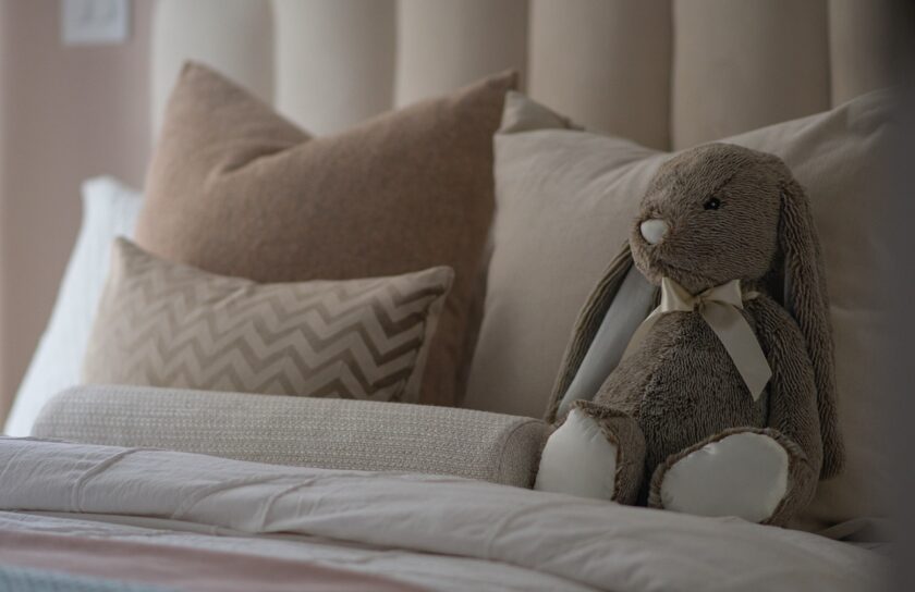 Gemütliches Bett mit weichen Kissen und einem beigefarbenen Kuschelhasen in ruhigen, neutralen Farbtönen