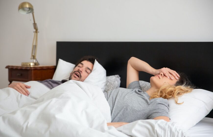 Ein Mann und eine Frau im Bett. Die Frau kann nicht schlafen, weil der Mann schnarcht
