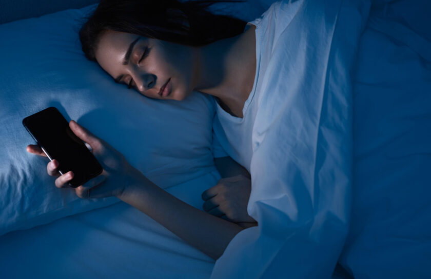 Schlafende Frau mit ausgeschaltetem Smartphone in der Hand im blauen Nachtlicht