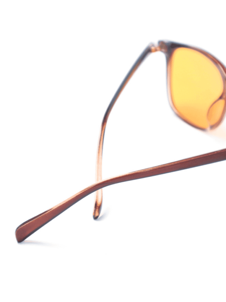Nahaufnahme einer Sonnenbrille mit braunem Rahmen und orangefarbenen Gläsern, überkreuzte Bügel auf weißem Hintergrund