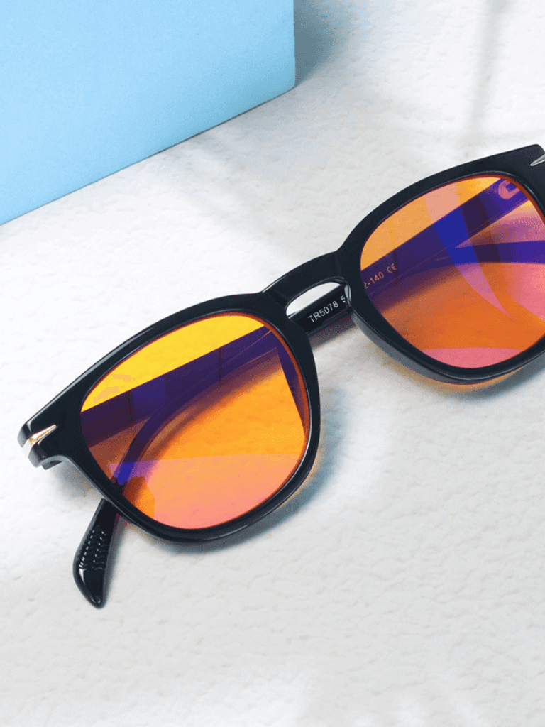 Schwarze Retro-Sonnenbrille mit orange-blau verspiegelten Gläsern auf heller marmorierter Oberfläche