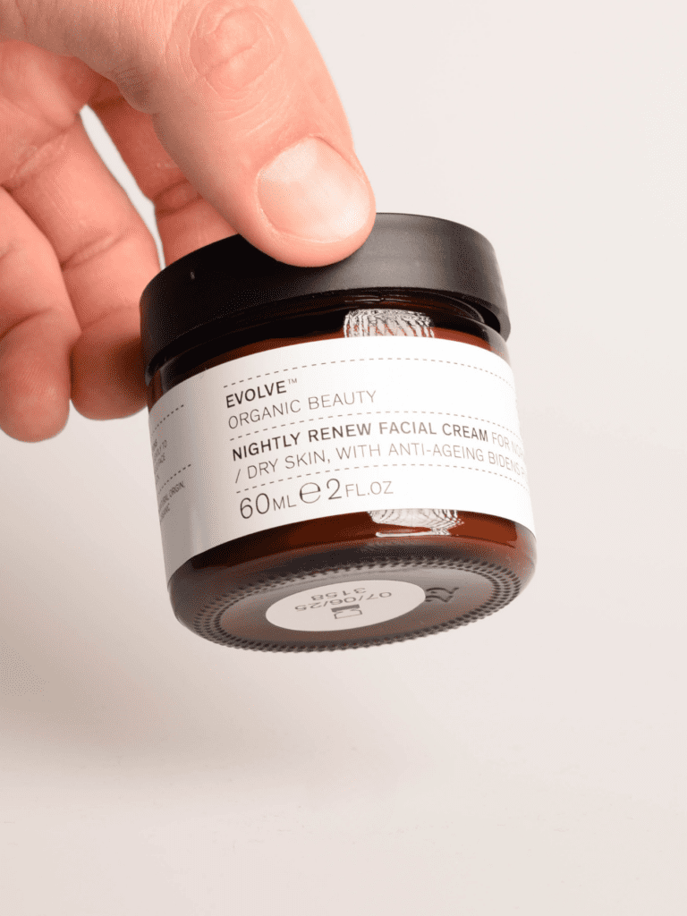 Hand hält einen braunen Kosmetiktiegel mit schwarzem Deckel und dem Etikett Evolve Nightly Renew Nachtcreme, 60 ml