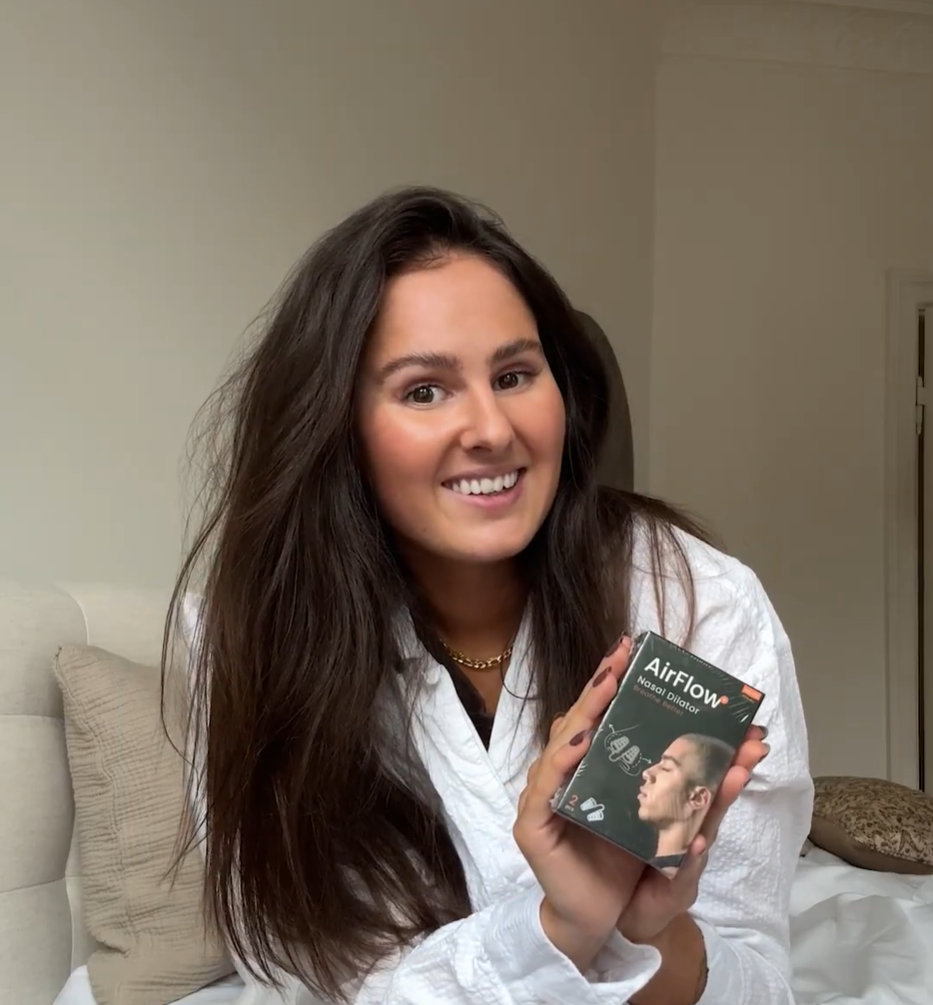 Lächelnde Frau hält eine AirFlow+ Nasendilatator-Packung, Nahaufnahme des Produkts im häuslichen Umfeld
