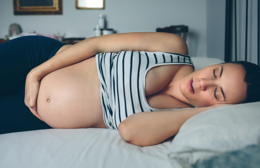 Schwangere Frau schläft im gestreiften Oberteil auf der Seite, die Hand auf dem Bauch