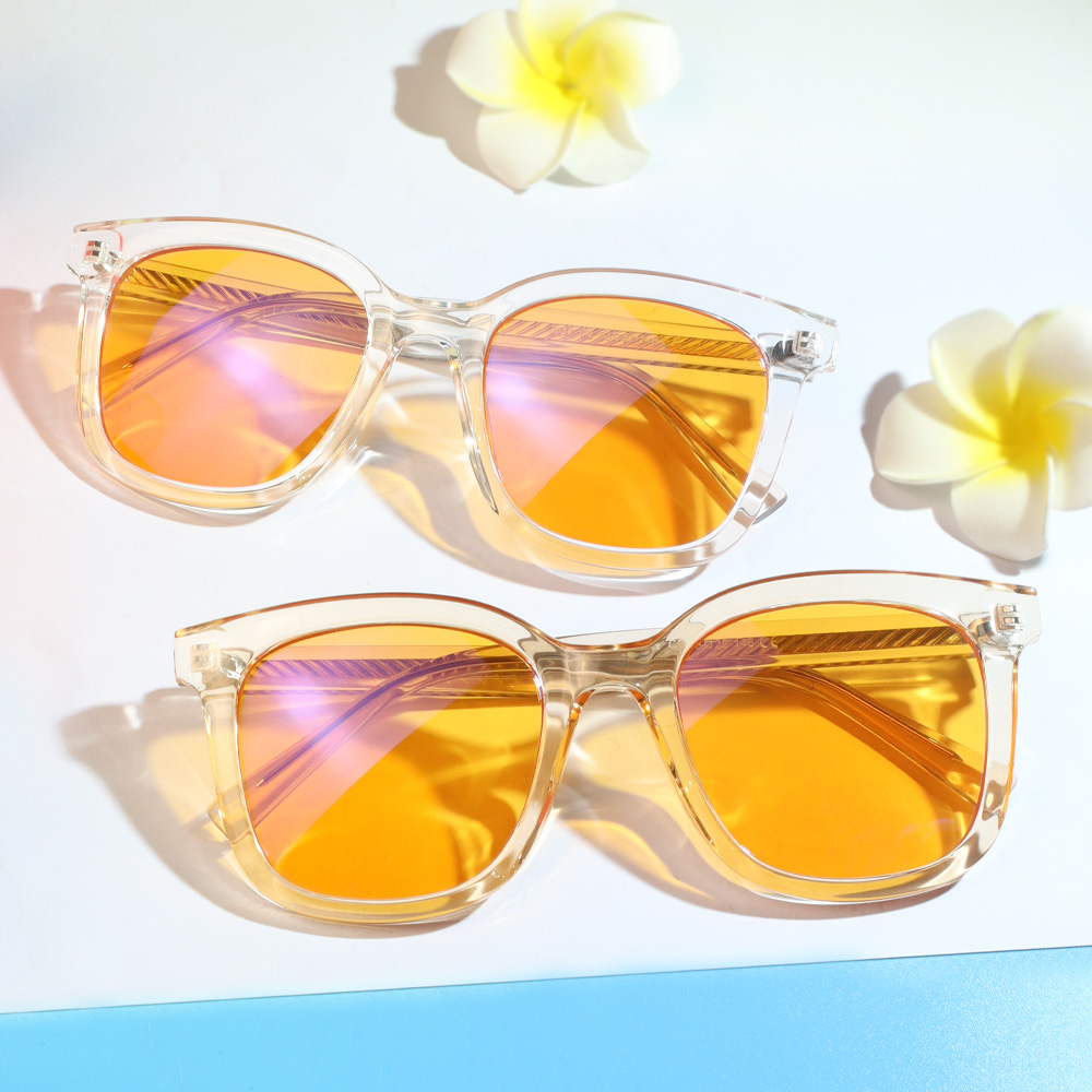 To transparente solbriller med orange-lilla spejlglas og plumeria-blomster på hvid baggrund