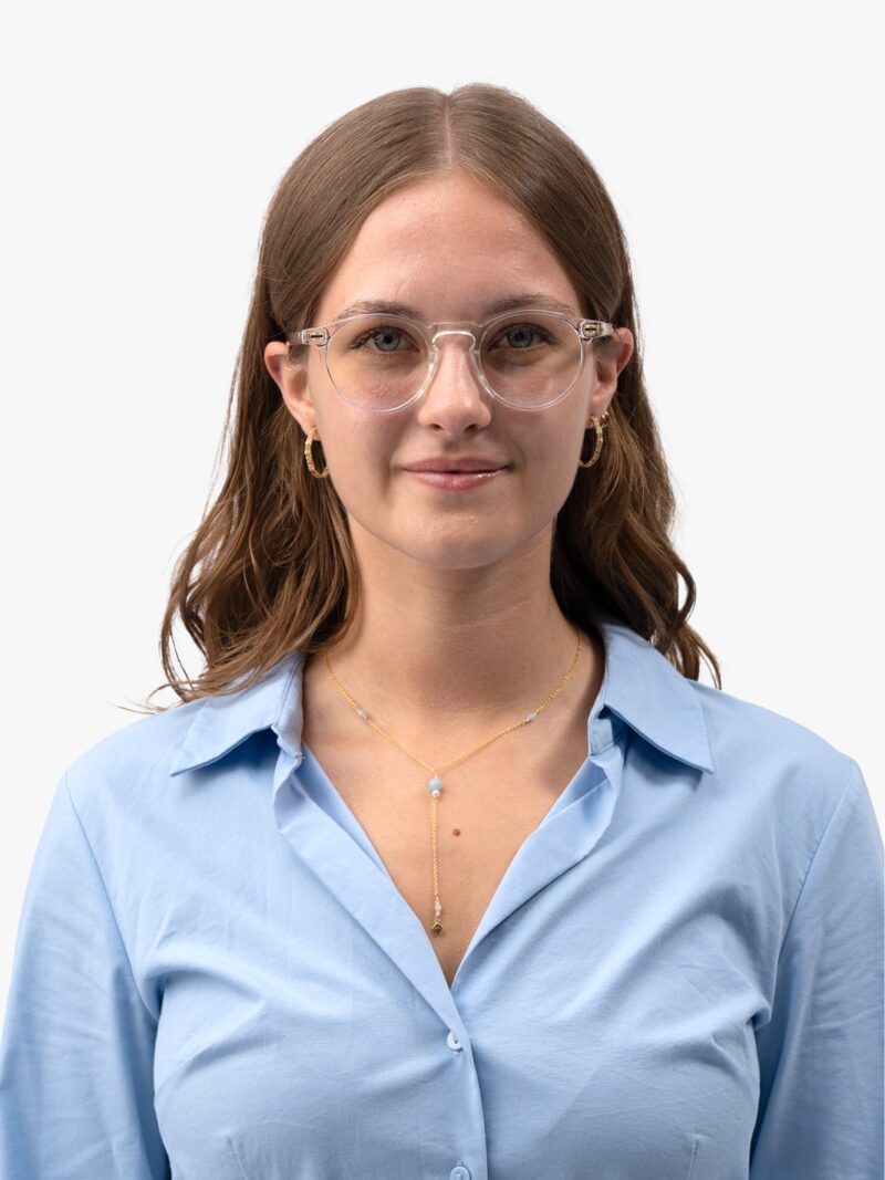 Frau im hellblauen Hemd mit transparenter runder Brille, goldener Lariat-Kette, Creolen und mittellangem braunem Haar