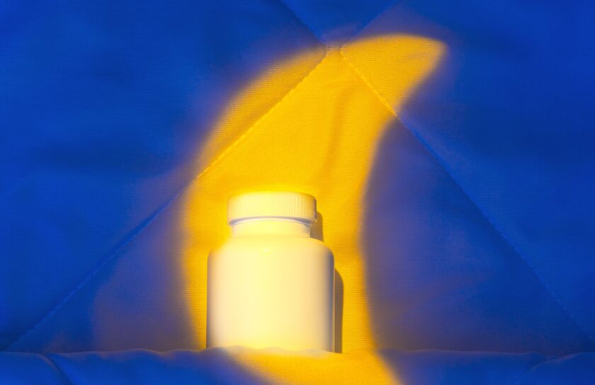 Weiße Melatonin-Dose auf einer Bettdecke, von warmem gelbem Licht beleuchtet vor blauem Hintergrund