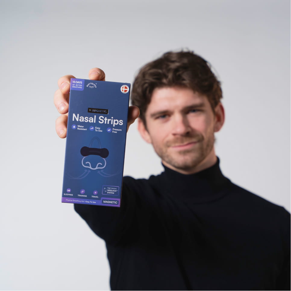 Mann im schwarzen Pullover hält eine blaue Schachtel Magnetic Nasal Strips mit Nasenillustration und Produkttext im Fokus