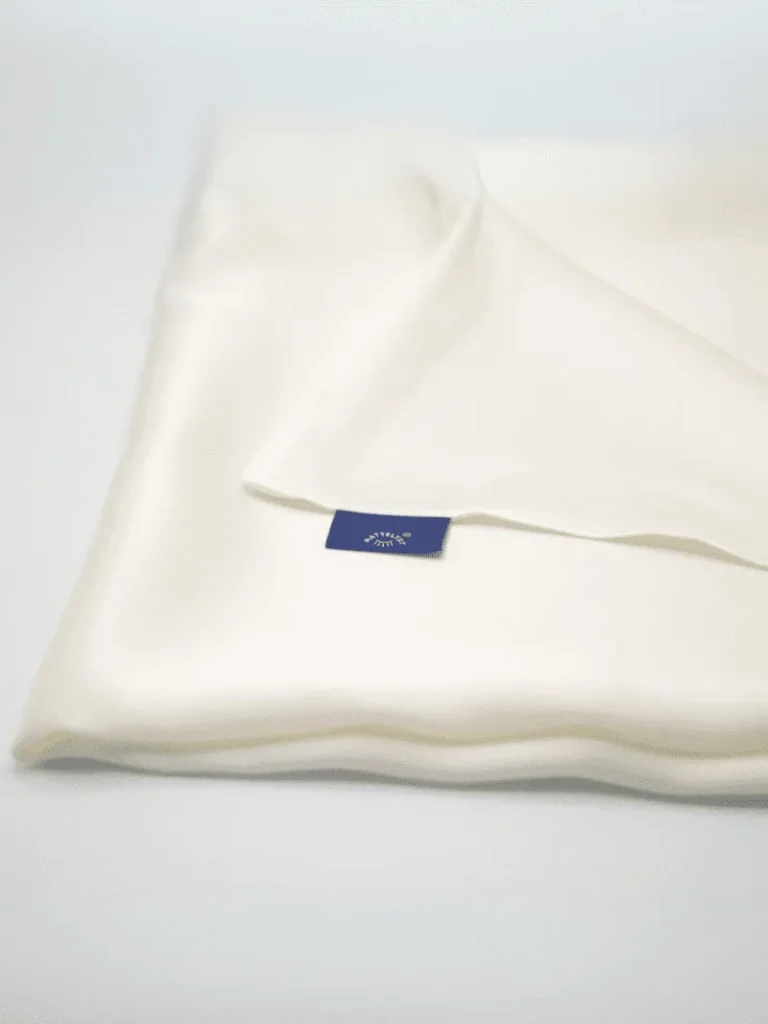 Gefalteter cremefarbener Seidenkissenbezug mit sichtbarem dunkelblauem Label