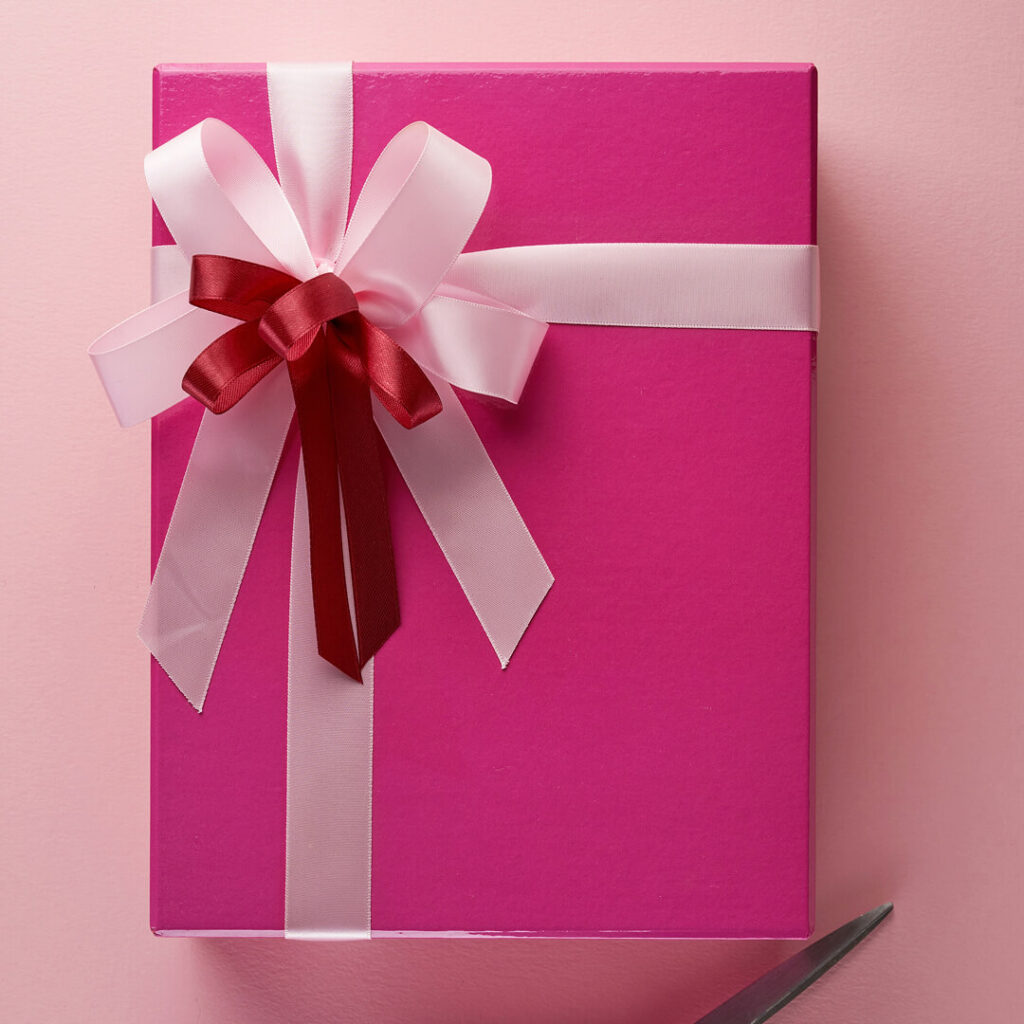 Rosa Geschenkbox mit rosa-roter Schleife auf rosafarbenem Hintergrund, Schere in der unteren Ecke