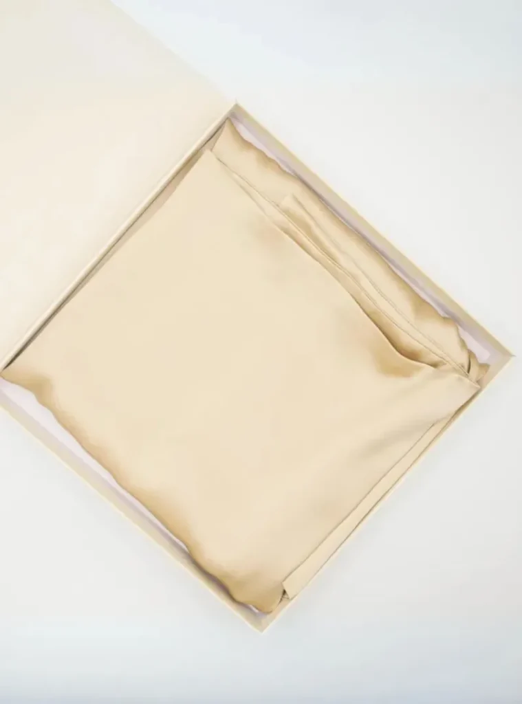 Beigefarbener Satin-Kissenbezug gefaltet in der Geschenkbox mit Seidenpapier