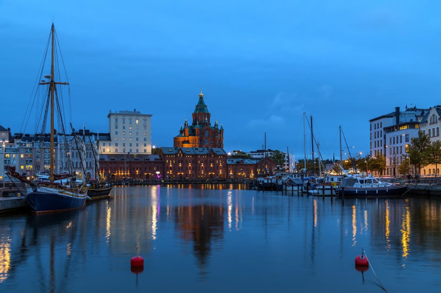 Abendlicher Hafen von Helsinki mit beleuchteter Uspenski-Kathedrale, Booten und Lichterreflexionen